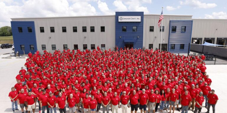 Un grand groupe en chemise rouge se tenant devant un bâtiment gris et bleu avec un drapeau américain.