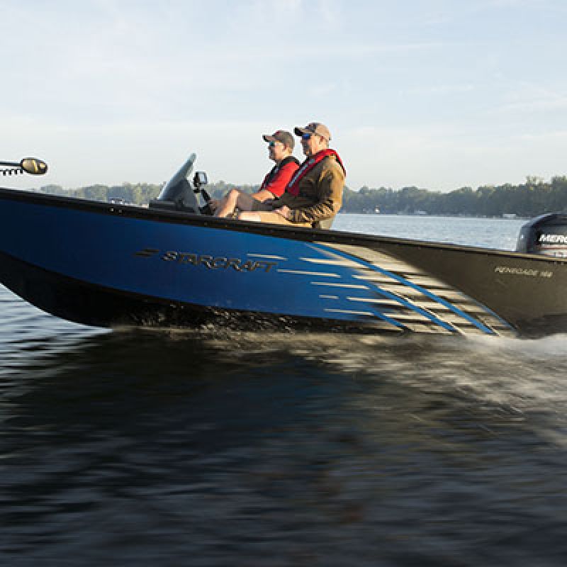 A blue motorboat with two people in life jackets moves across calm water.