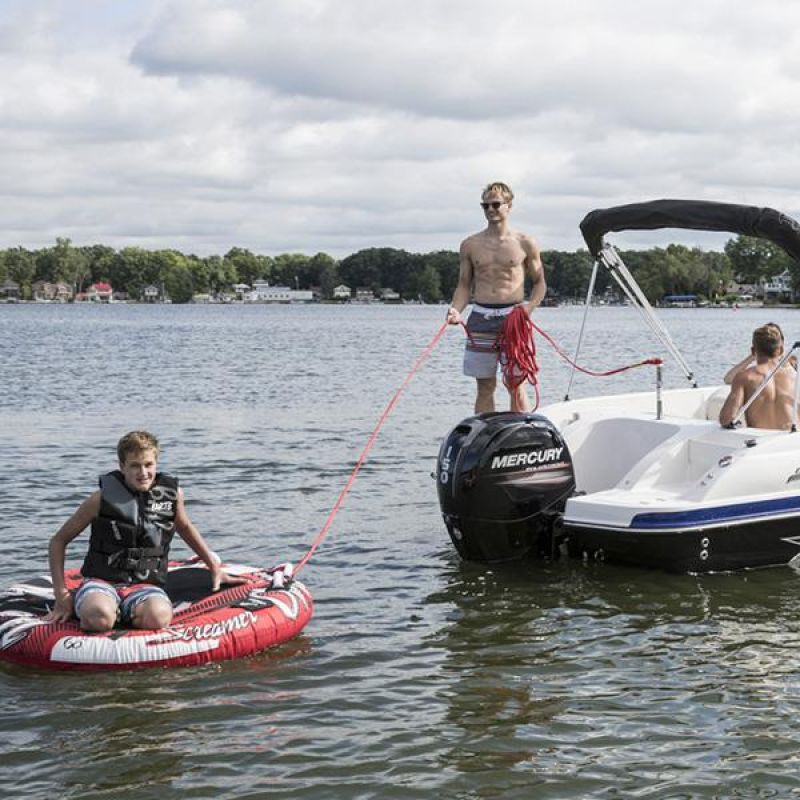 A motorboat on a lake with a person pulling a child on a red inflatable tube.